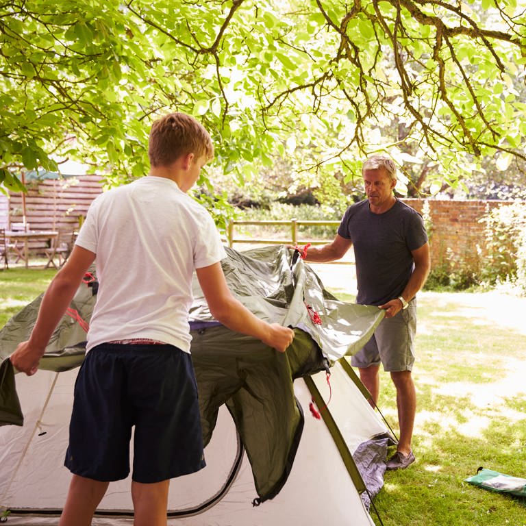 Vater und Sohn bauen in einem Garten ein Zelt auf.
