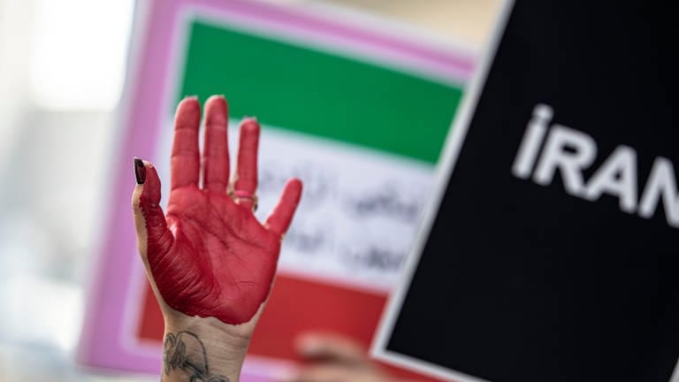 Die rot bemalte Hand einer Demonstrantin erhebt sich zwischen Plakaten während einer Demonstration vor dem iranischen Konsulat. Nach dem Tod einer 22-jährigen in Teheran kommt es weltweit zu Protesten und Solidaritätskundgebungen. (Foto: dpa Bildfunk, Picture Alliance)