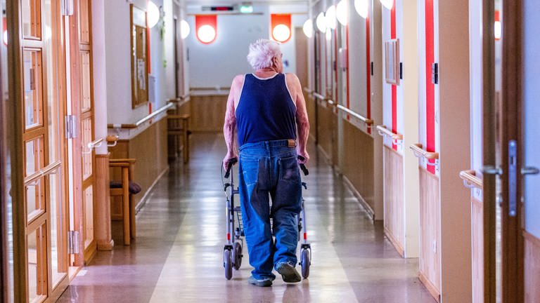 Pflegebedürftiger Senior im Altenheim schiebt Rollator durch einen leeren Flur