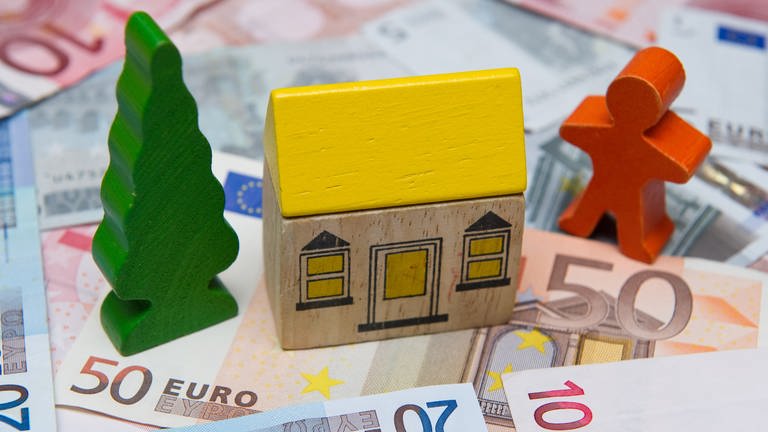 Ein kleines Spielzeughaus auf Geldscheinen (Sujet: Immobilien-Preisspiegel 2023)