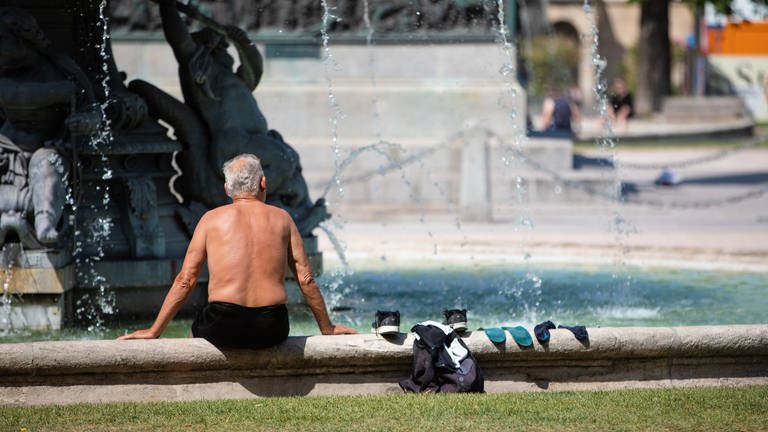 Ein Mann steckt bei heißen Temperaturen seine Füße in einen Brunnen, um sich abzukühlen