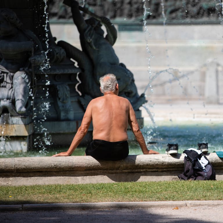Ein Mann steckt bei heißen Temperaturen seine Füße in einen Brunnen, um sich abzukühlen (Foto: dpa Bildfunk, picture alliance/dpa | Christoph Schmidt)