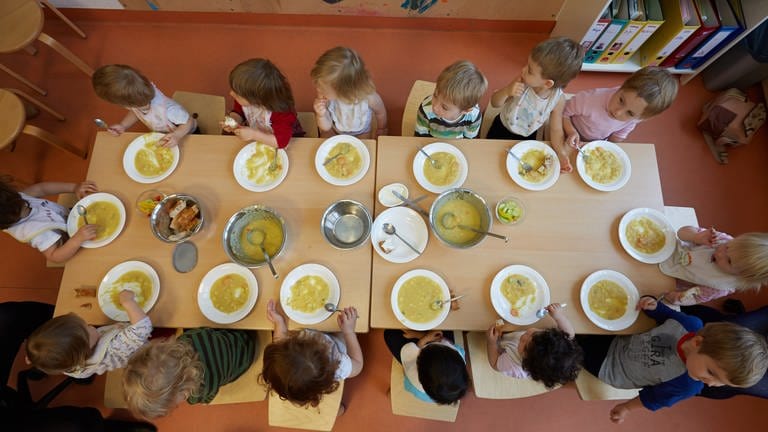 Kinder in einer Kita sitzen gemeinsam an einem Tisch beim Mittagessen.