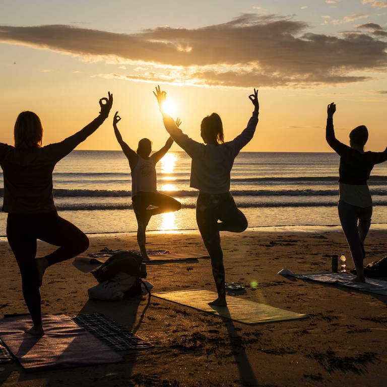 Yoga-Klasse übt bei Sonnenuntergang am Strand (Foto: dpa Bildfunk, Picture Alliance)
