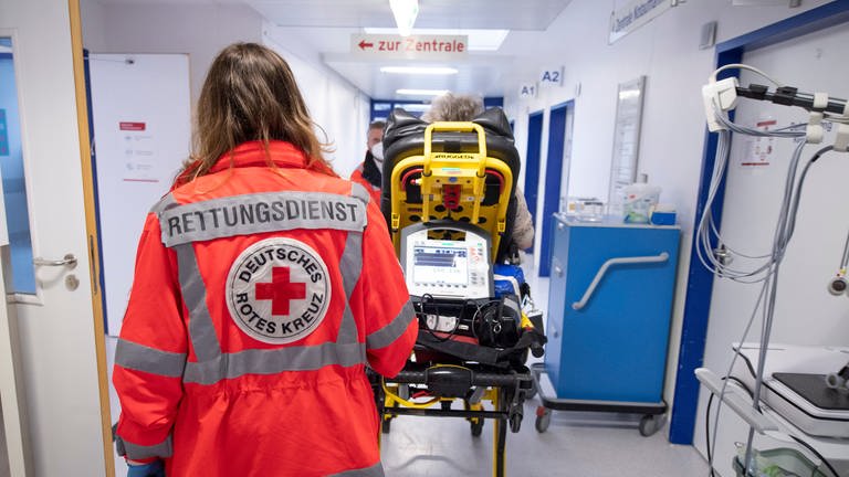 Notfallsanitäterin des Deutschen Roten Kreuzes (DRK) schiebt eine Seniorin nach einem Schlaganfall auf einer Trage in die Notaufnahme eines Krankenhauses. 