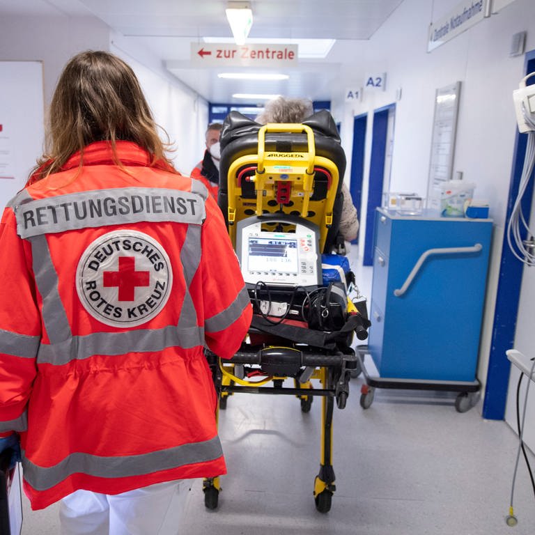 Notfallsanitäterin des Deutschen Roten Kreuzes (DRK) schiebt eine Seniorin nach einem Schlaganfall auf einer Trage in die Notaufnahme eines Krankenhauses. 