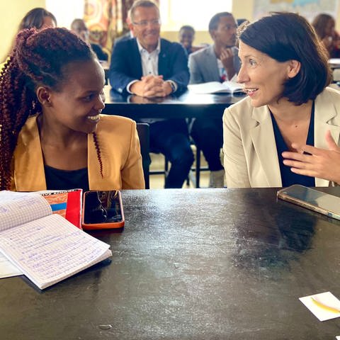 Wirtschaftsministerin Daniela Schmitt sitzt neben einer jungen Frau aus Ruanda, die einen Deutsch-Kurs besucht. 