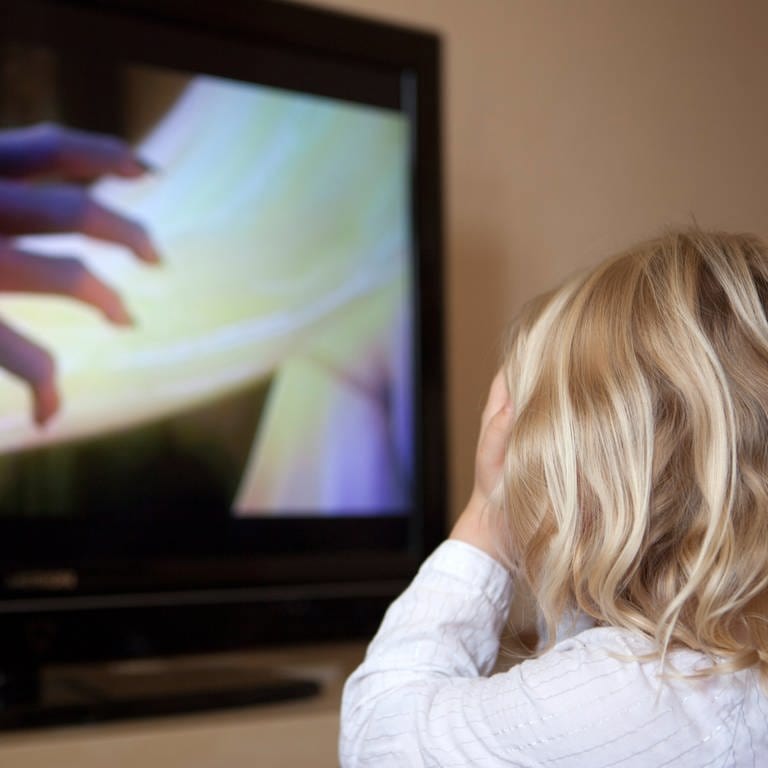 Ein Kind sitzt vor einenm Fernseher auf dem Ein Horrorfilm läuft und hält sich die Augen zu.