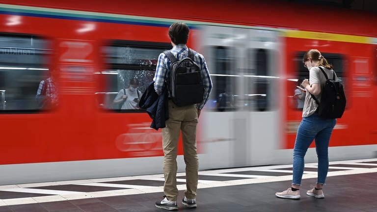 Zwei Menschen stehen an einem Bahnsteig, als ein Zug einfährt.