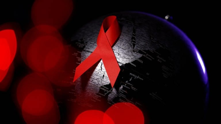 Es ist das für AIDS bekannte Symbol der roten Schleife zu sehen, auf einem schwarzen Hintergrund.