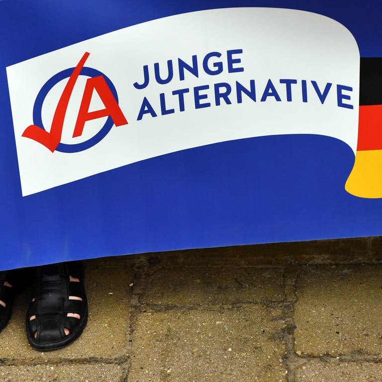 Ein Mann in schwarzen Sandalen hält ein Plakat der AfD-Jugendorganisation Junge Alternative (JA) (Foto: dpa Bildfunk, picture alliance/dpa/dpa-Zentralbild | Jens Kalaene)