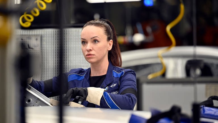 Fachkräftegewinnung geglückt: Eine junge Frau steht in der Werkhalle eines Autobauers an einer Maschine 
