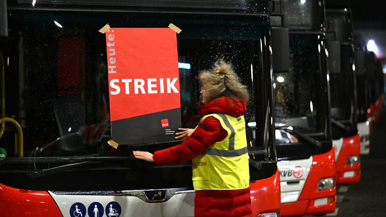 Eine Mitarbeiterin klebt ein Plakat mit der Aufschrift "Streik" auf die Frontscheibe eines Busses.  (Foto: dpa Bildfunk, picture alliance/dpa | Federico Gambarini)