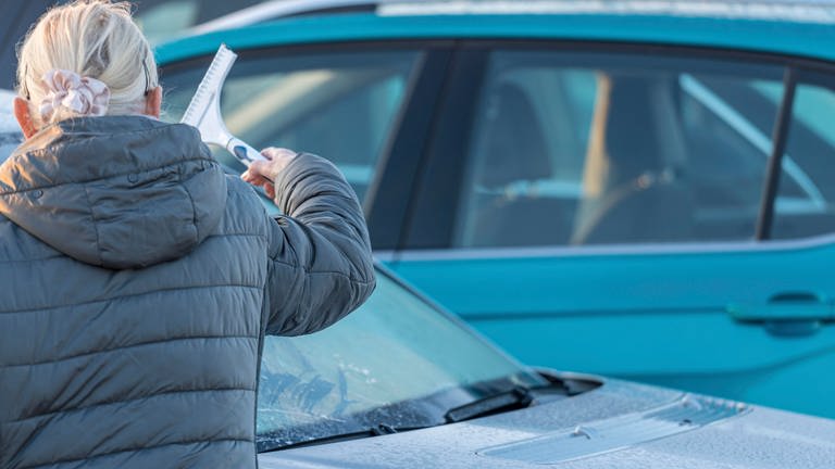 ältere Frau kratzt mit einem Eiskratzer die Windschutzscheibe ihres Auto frei. Scheibe von Schnee und Eis befreien (Foto: dpa Bildfunk, picture alliance / CHROMORANGE | Michael Bihlmayer)