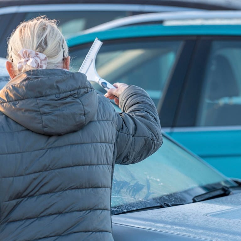 Das Wetter bleibt kalt: Eine ältere Frau kratzt in RLP mit einem Eiskratzer die Windschutzscheibe ihres Auto frei. Der April-Winter hat Rheinland-Pfalz weiter im Griff.
