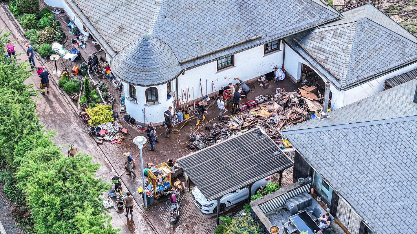 Das Luftbild zeigt Aufräumarbeiten in Kirn-Sulzbach am Tag nach dem Regen. Menschen kämpfen gemeinsam gegen Schlamm und Wasser an. (Foto: dpa Bildfunk, picture alliance/dpa | Jason Tschepljakow)