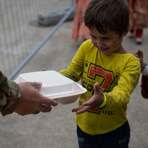 Ein kleiner Jungen erhält auf der Air Base Ramstein von einem US-Soldaten eine Plastikbox mit Essen.  (Foto: Pressestelle, Ramstein Air Base/Milton Hamilton/86th Airlift Wing/Public Affairs)