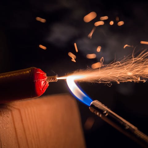 Eine Flamme entzündet die Zünmdschnur eines Böllers und es schlagen Funken.  (Foto: dpa Bildfunk, Picture Alliance)
