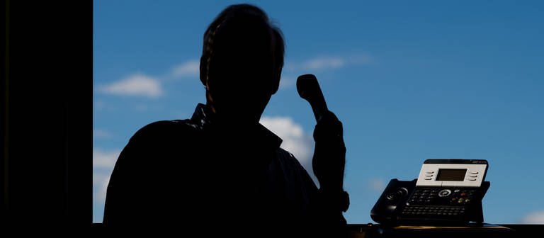Ein Mann steht vor einem Fenster und hält ein Telefon in der Hand. (Foto: picture-alliance / Reportdienste, picture alliance / Julian Stratenschulte/dpa | Julian Stratenschulte)