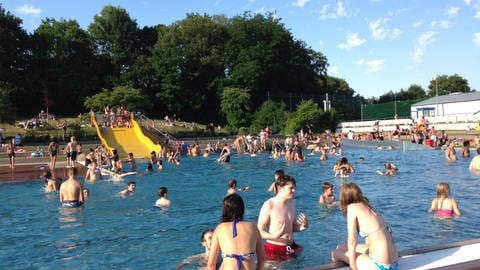 Viele Menschen im Becken eines Freibades, im Hintergrund eine gelbe Rutsche (Foto: SWR)