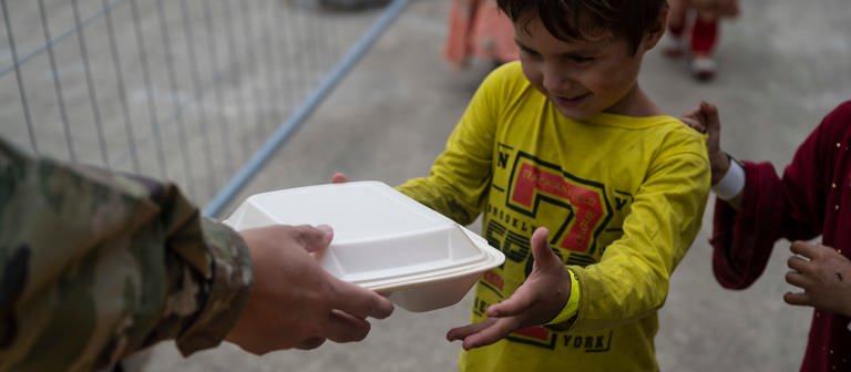 Ein kleiner Jungen erhält auf der Air Base Ramstein von einem US-Soldaten eine Plastikbox mit Essen.  (Foto: Pressestelle, Ramstein Air Base/Milton Hamilton/86th Airlift Wing/Public Affairs)