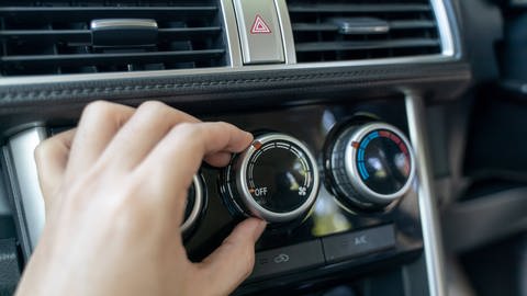Eine Klimaanlage in einem Auto, eine Hand dreht am Regler. (Foto: IMAGO, IMAGO / YAY Images)