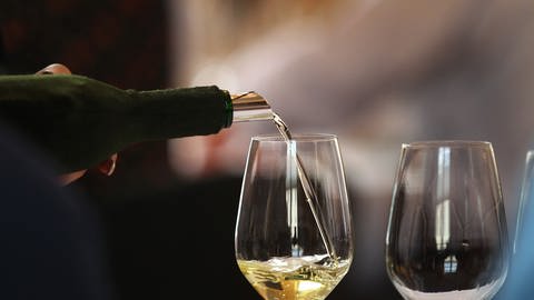 Aus einer Weinflasche wird Weißwein in ein Glas geschüttet