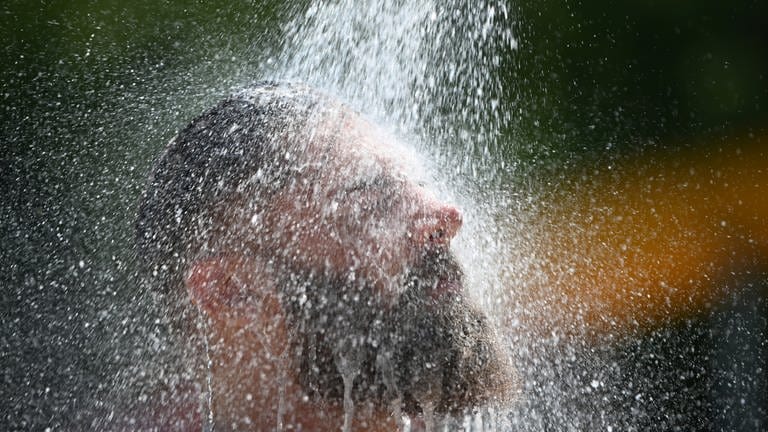 Ein Mann kühlt sich im Freien unter Wasser ab. (Foto: dpa Bildfunk, picture alliance/dpa | Patrick Seeger)