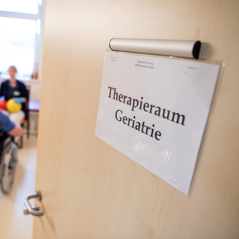 Eine Zimmertür in einer Klinik steht offen. An der Tür hängt ein Schild mit der Aufschrift "Therapieraum Geriatrie". (Foto: dpa Bildfunk, picture alliance/dpa | Daniel Bockwoldt)