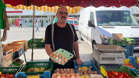 Landwirt Ralf Folz hält eine Schachtel mit Eiern in die Kamera und steht an seinem Marktstand (Foto: SWR)
