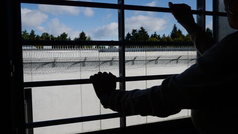 Insasse steht hinter vergittertem Fenster und schaut Gefängnismauer.  (Foto: picture-alliance / Reportdienste, Picture Alliance)
