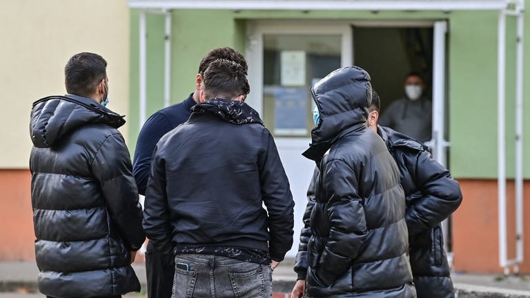 Eine Gruppe Flüchtlinge in dunklen Jacken steht zusammen vor einer Erstaufnahmeeinrichtung