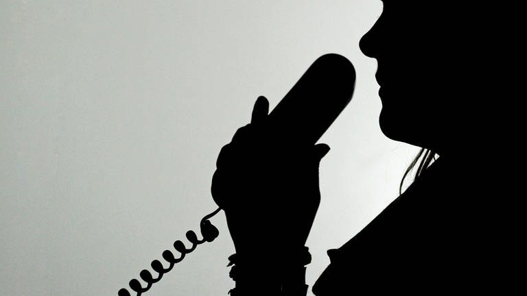 Polizei Kaiserslautern registriert zahlreiche Schockanrufe - eine Frau im Schatten hält einen Telefonhörer (Foto: picture-alliance / Reportdienste, picture alliance / dpa | Jan-Philipp Strobel)