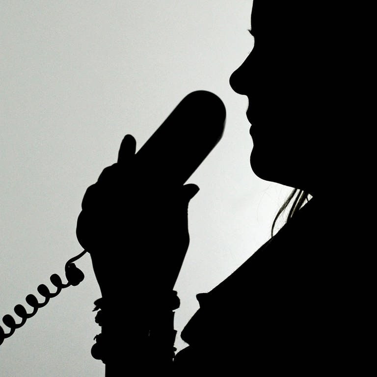 Polizei Kaiserslautern registriert zahlreiche Schockanrufe - eine Frau im Schatten hält einen Telefonhörer