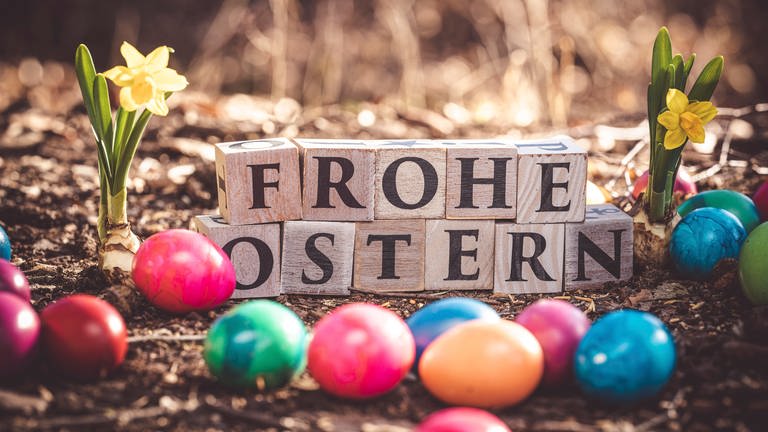 Frohe Ostern geschrieben mit Holzwürfeln, bunte Eier und Narzissen
