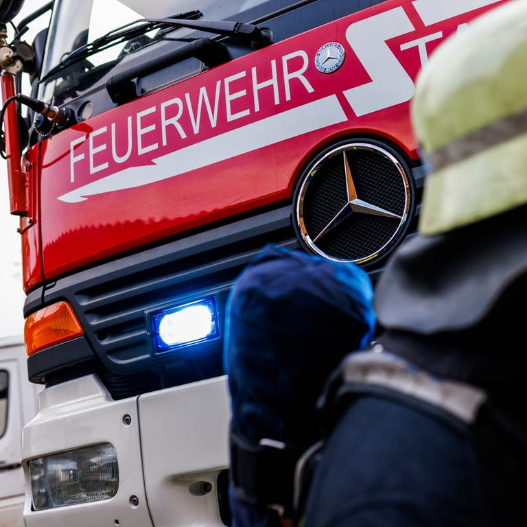 Ein Einsatzfahrzeug der Feuerwehr und davor steht ein Feuerwehrmann in Atemschutzmaske. (Foto: picture-alliance / Reportdienste, picture alliance_dpa_Philipp von Ditfurth)