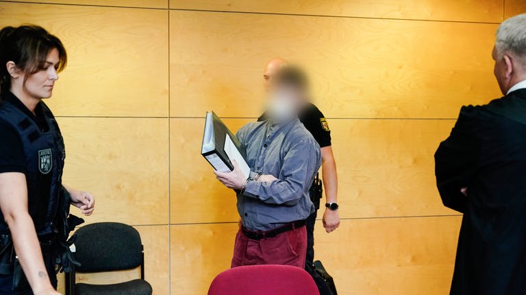 Der 39-jährige Hauptangeklagte im Fall der getöteten Polizisten im Kreis Kusel kommt mit Handschellen in den Verhandlungssaal des Landgerichts Kaiserslautern.