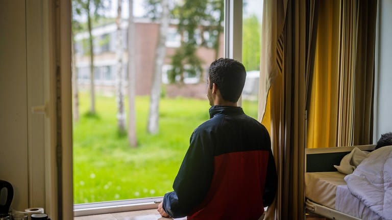 Ein Flüchtling, der von seinem Zimmer aus durch ein Fenster in den Garten schaut. 