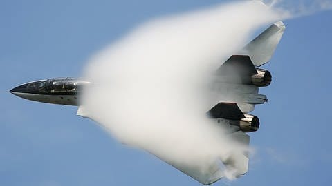 Ein Kampfjet fliegt mit Überschallgeschwindigkeit und durchbricht gerade die Schallmauer.