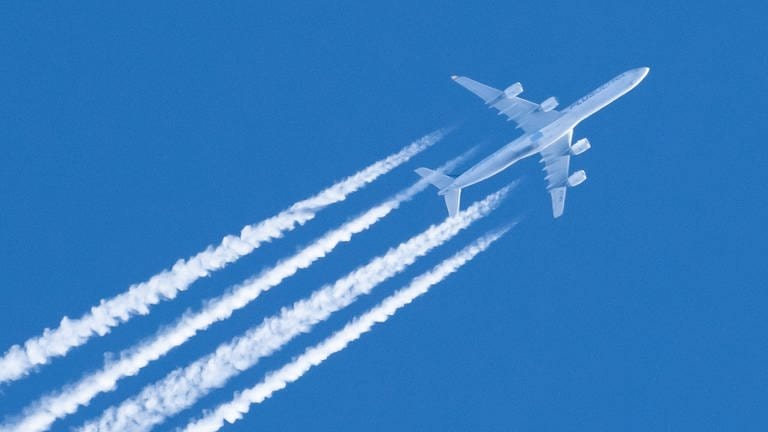 Ein Flugzeug fliegt am Himmel und hinterlässt Kondensstreifen (Foto: IMAGO, IMAGO/Silas Stein)