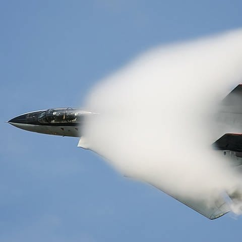 Ein Kampfjet fliegt mit Überschallgeschwindigkeit und durchbricht die Schallmauer.