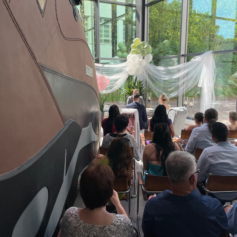 Die Hochzeitsgäste und das Brautpaar sitzen direkt neben dem größten Schuh der Welt bei der Trauung. (Foto: SWR)
