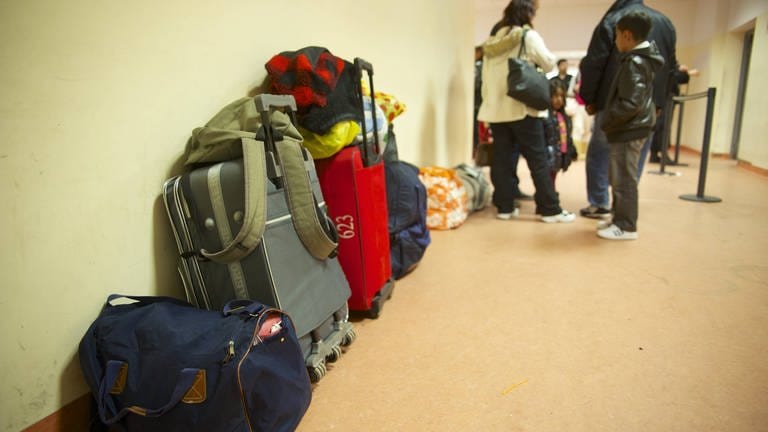 Eine Flüchtlingsfamilie wartet samt Gepäck in einer Aufnahmeeinrichtung.