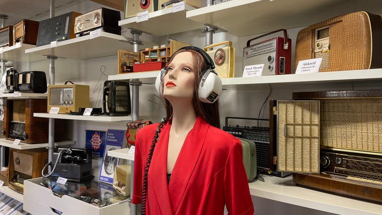 Frau mit Kopfhörer steht vor mehreren alten Radios - 100 Jahre Radio im Radiomuseum in Obermoschel (Foto: SWR)