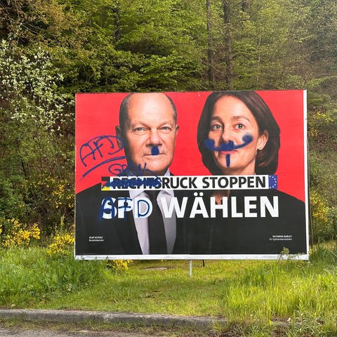 Das bemierte Wahlplakat der SPD in Münchweiler zeigt Bundeskanzler Olaf Scholz mit einem Hitler-Bart. Die Schmierereien rufen dazu auf die AfD zu wählen. 