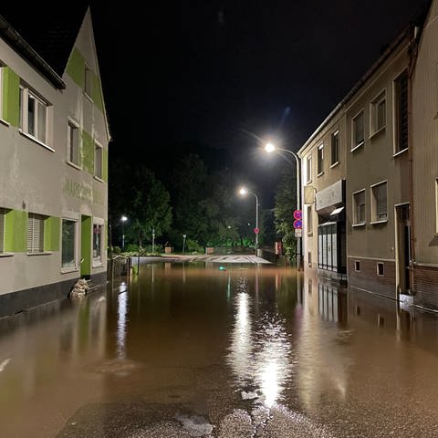 Eine Straße zwischen zwei Häusern in Waldfischbach-Burgalben ist überschwemmt. 