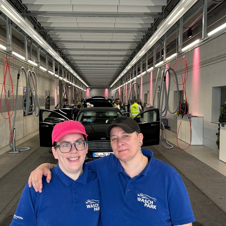 Zwei Mitarbeiterinnen des inklusiven "Waschparks" in Kaiserslautern stehen am Ende eines Fließbands, worauf die Autos von Mitarbeitern innen gereinigt werden. (SWR)