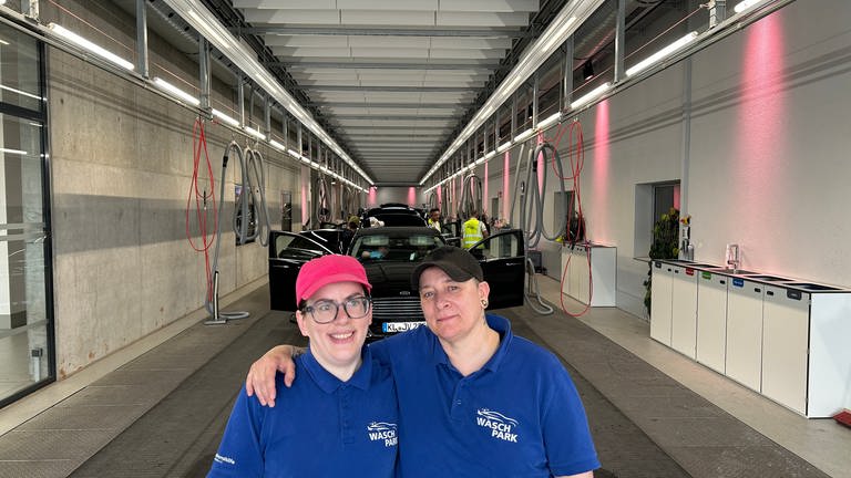 Zwei Mitarbeiterinnen des inklusiven "Waschparks" in Kaiserslautern stehen am Ende eines Fließbands, worauf die Autos von Mitarbeitern innen gereinigt werden. (SWR)