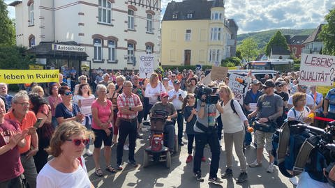 Viele Menschen sind auf einem Platz in Bad Neuenahr-Ahrweiler versammelt. Sie halten zum Teil Transparente hoch. Die Betroffenen der Flutkatastrophe demonstrieren. Der Wiederaufbau geht ihnen zu langsam. (Foto: SWR)