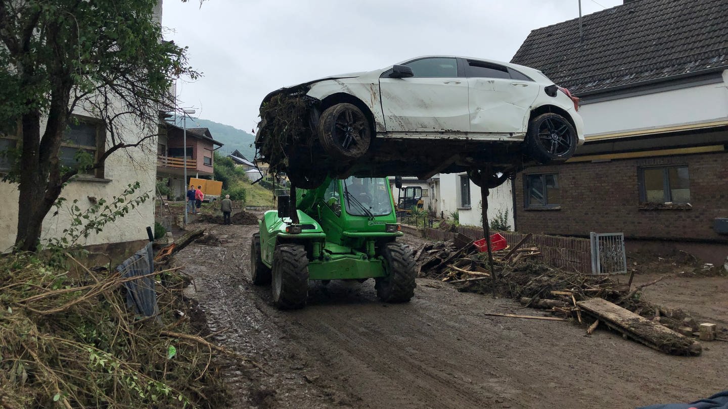 Ein kleiner Traktor fährt ein kaputtes Auto weg in Schuld nach dem Hochwasser der Ahr
